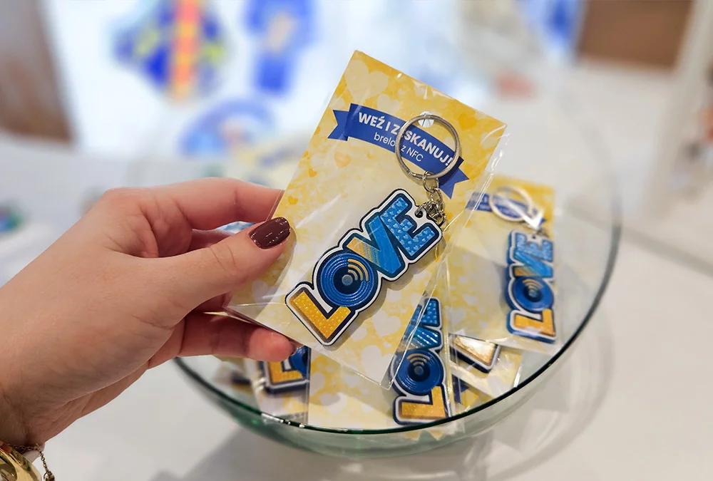 LOVE keychain with NFC held in hand on a dedicated card, with the rest in a glass container, at the DECARD booth during PROMO SHOW 2026