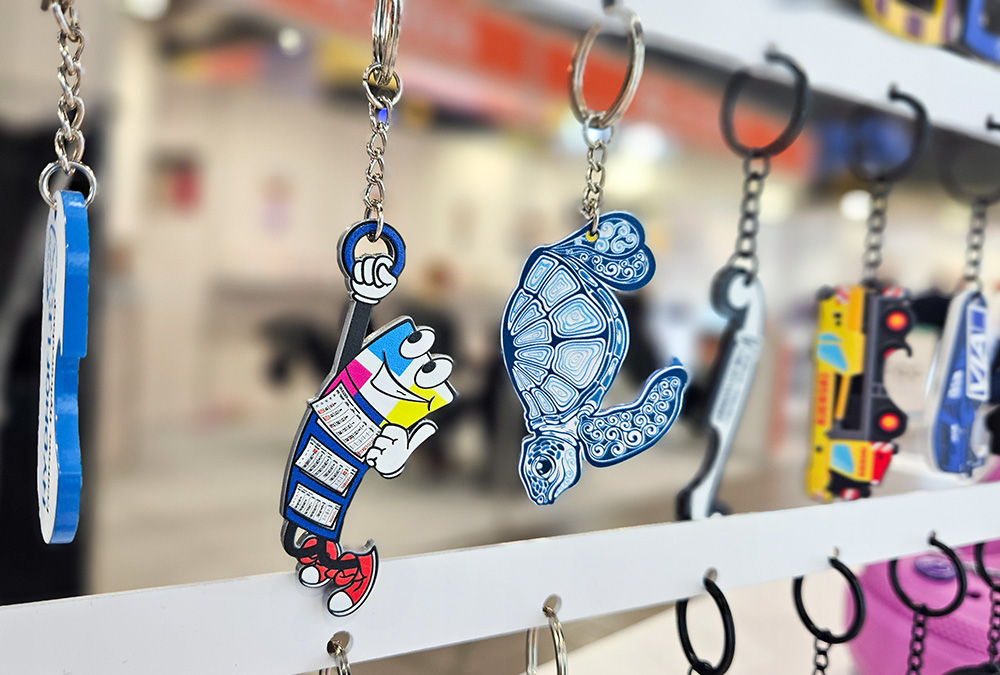 Keychains with bottle opener function – metal, colorful calendar, turtle, vehicles – hanging at the DECARD booth during PROMO SHOW 2026