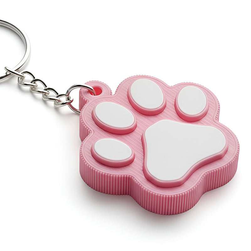 Close-up of a 3D keychain in the shape of an animal paw – visible raised paw pads on the front, decorative 3D patterns along the edges, and vivid pastel colors with a resin texture. Manufactured in Poland by DECARD