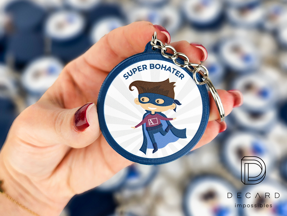 Keychain with a superhero “Brave Patient,” held in hand against the background of other keychains from this series, made by the Polish manufacturer DECARD