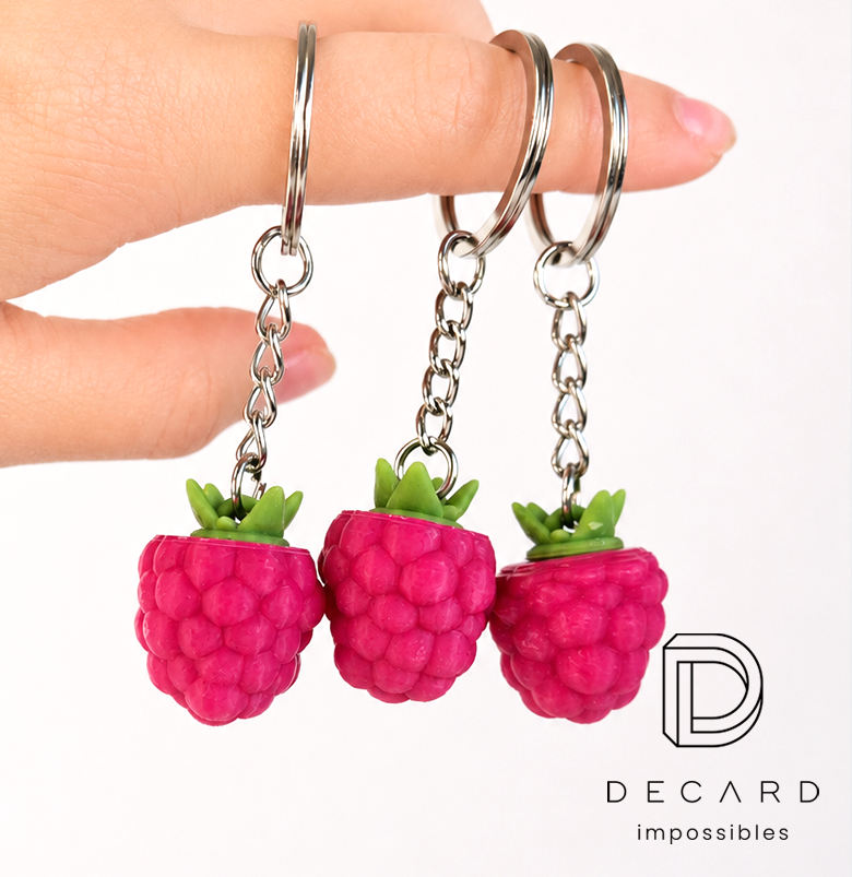 3D raspberry keychains with a green leaf, held in a hand on silver attachments, made by Polish manufacturer DECARD
